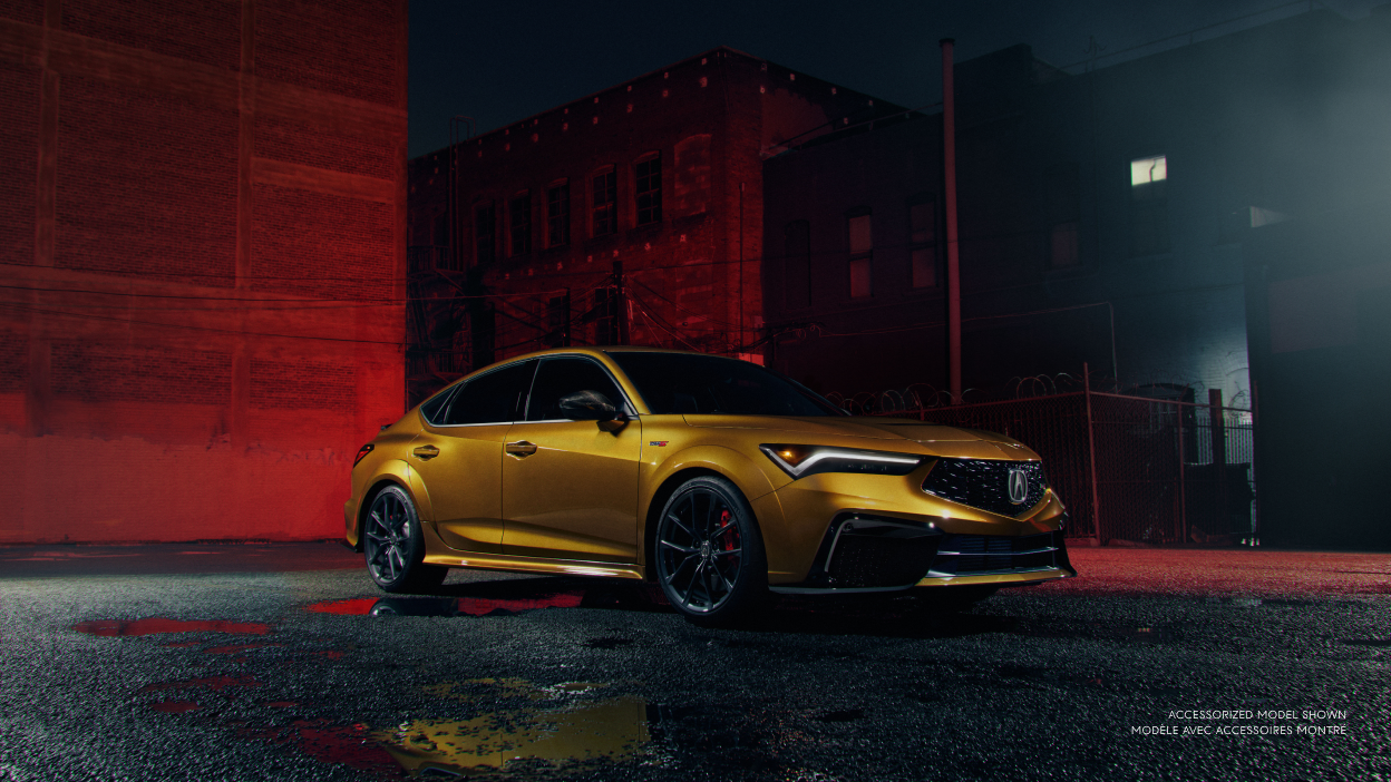 Plan de trois quarts avant d’une Integra Type S de couleur or stationnée dans une ruelle devant un mur éclairé par une lumière rouge.