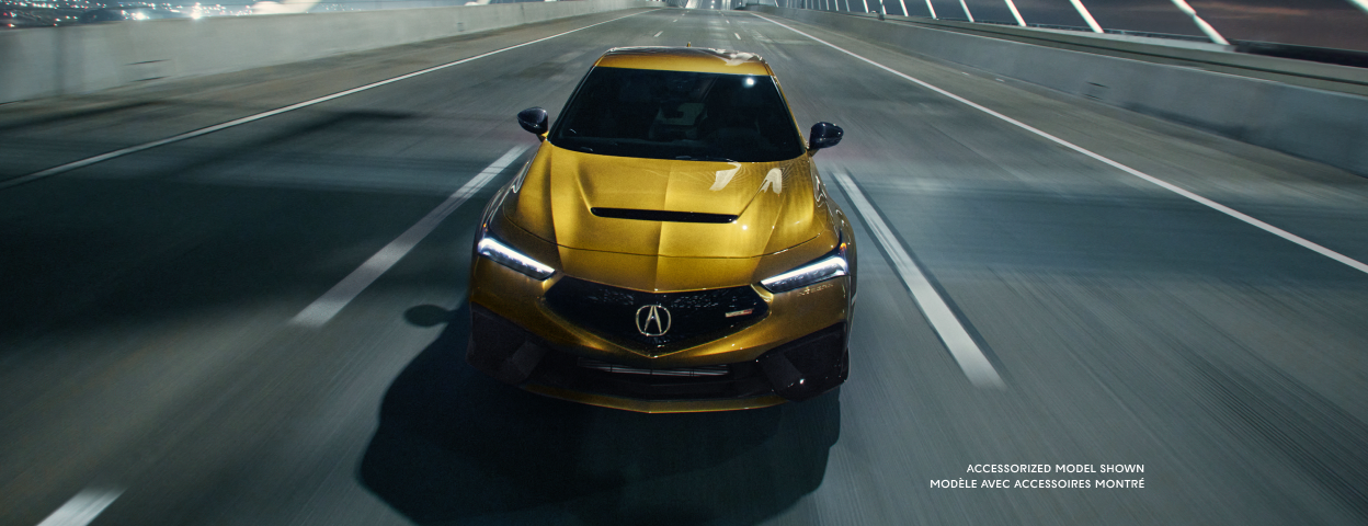 3/4 front bird’s eye view of a gold Integra Type S driving over bridge at night.