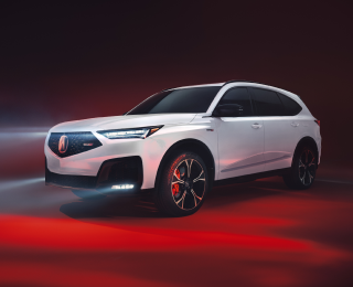 3/4 side front view of white MDX, with its headlights on, in a studio lit with red light.