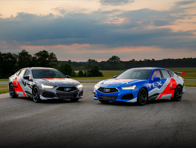 A grey and a blue Acura TLX, both with red and grey sponsorship wraps, parked slightly facing each other in front of an open field with trees in the background.	Deux Acura TLX, l’une grise et l’autre bleue, recouverte d’un habillage personnalisé rouge et gris, stationné en angle l’une en face de l’autre devant un terrain gazonné et des arbres.